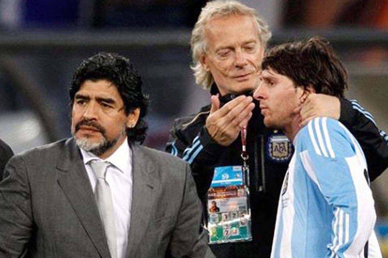 Maradona, coach, with Messi, athlete, on field. Man in black vest behind Messi.