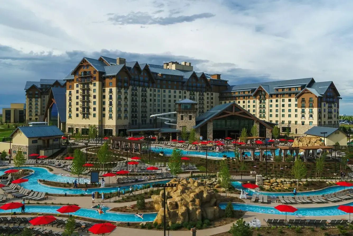 Resort with water park: large building with pool and lazy river, blue water, red umbrellas.