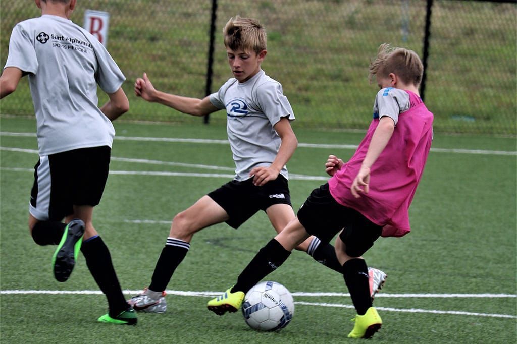Boys in soccer jerseys playing soccer on a green field. One kicks the ball, others nearby.