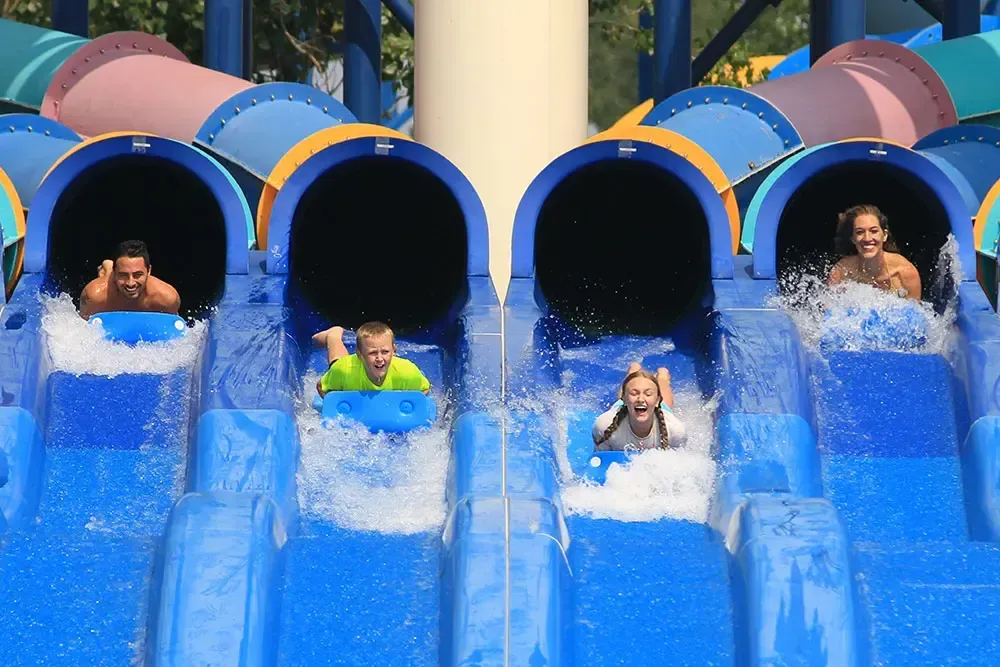 People sliding down blue water slides at a water park, splashing water, smiling.
