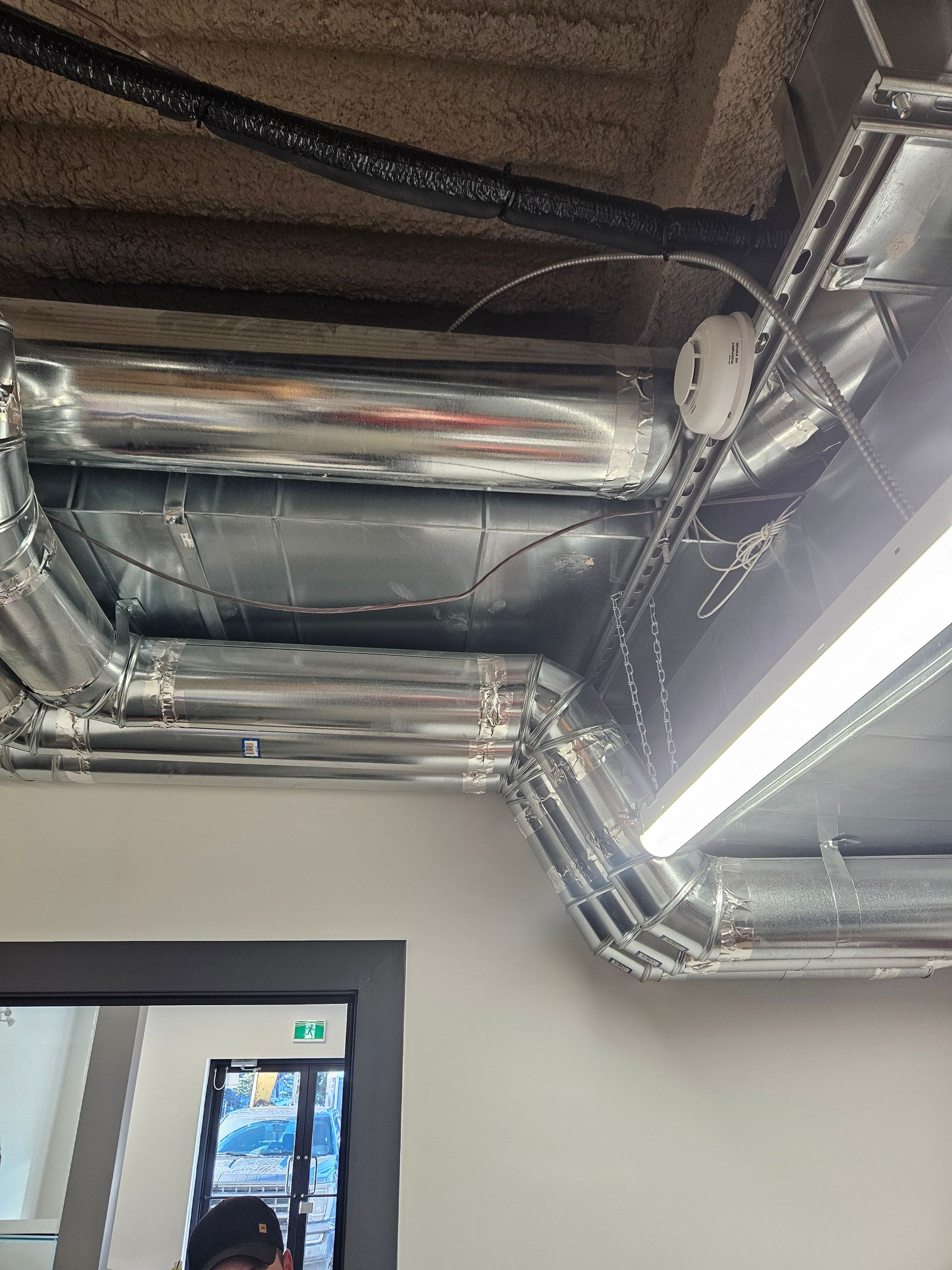 Un homme se tient dans une pièce avec beaucoup de tuyaux suspendus au plafond.