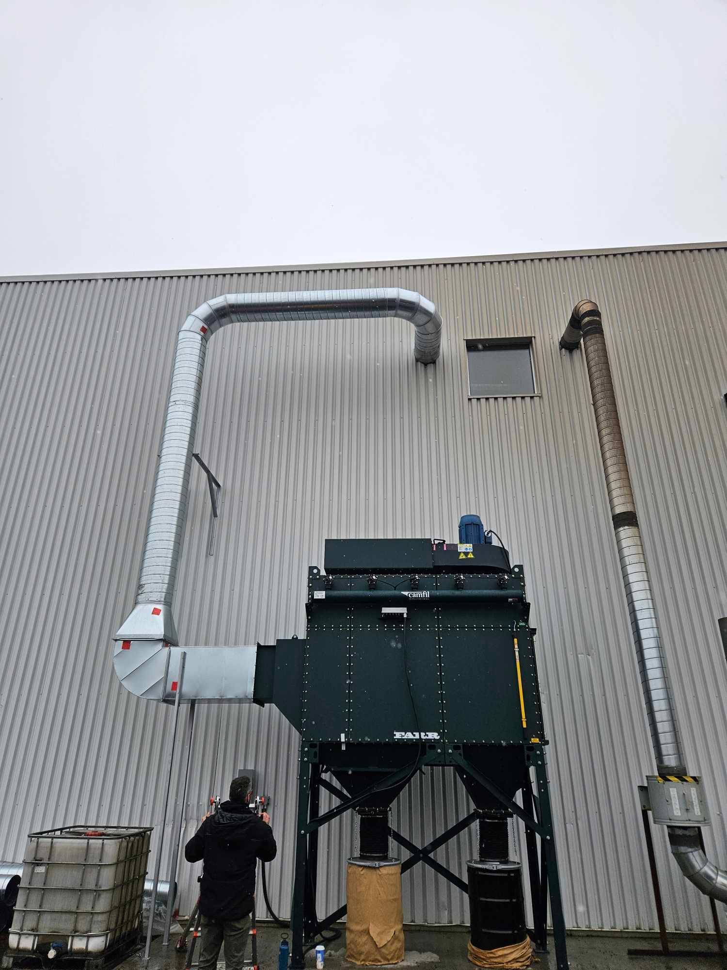 Un homme se tient devant un grand bâtiment auquel est attaché un tuyau.