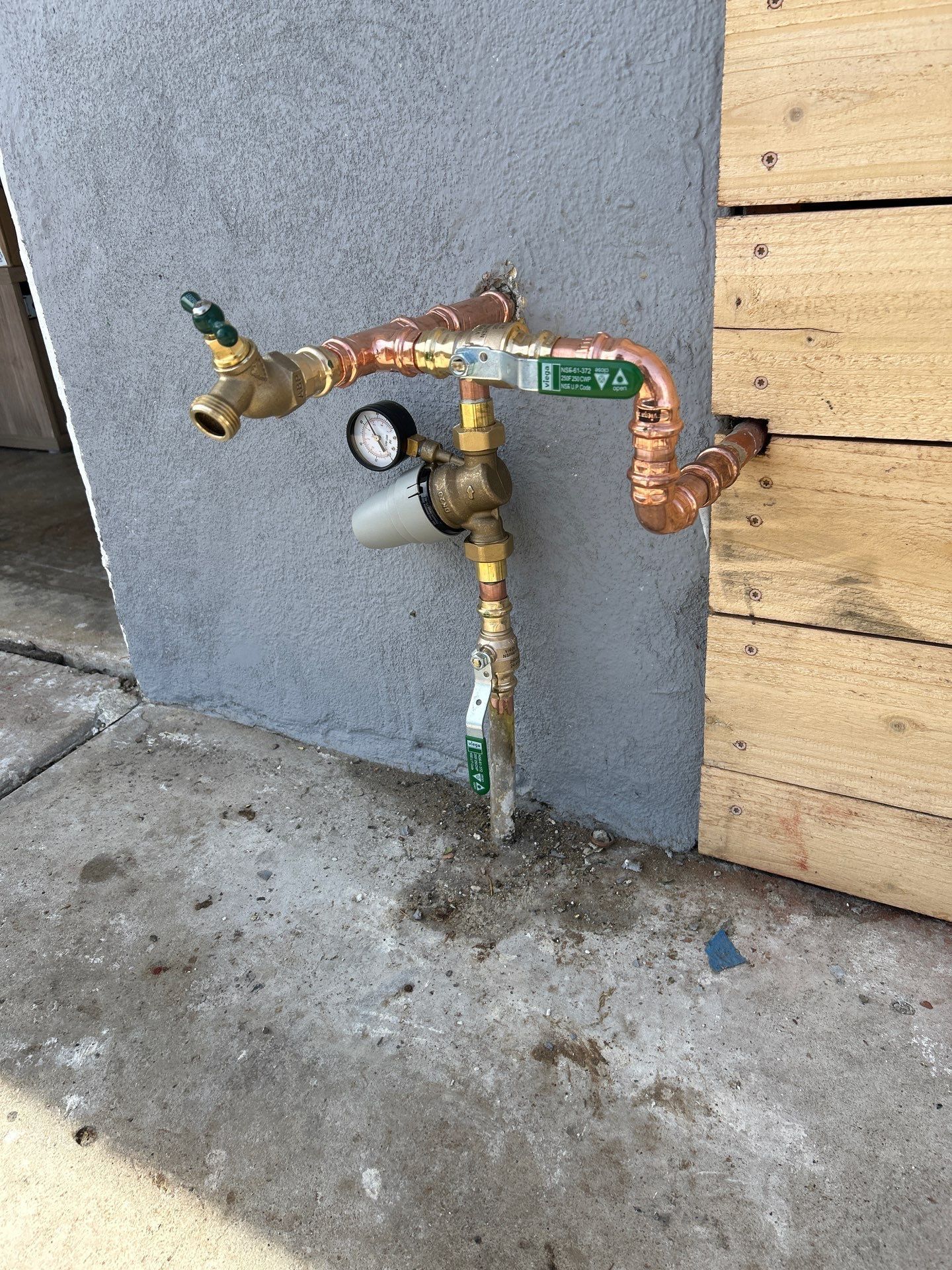 Pride Plumbing, Inc | A faucet with a gauge attached to it is sitting on the sidewalk next to a wooden wall.