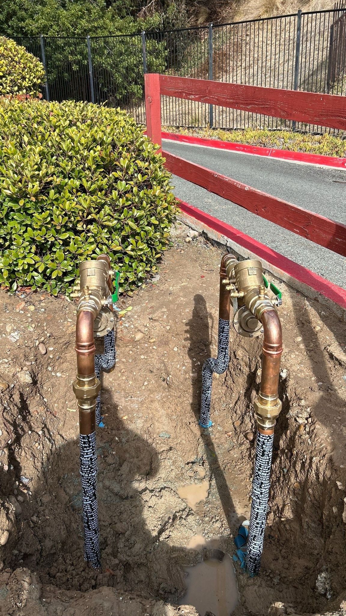 Pride Plumbing, Inc | A couple of copper pipes sitting in the dirt next to a fence.
