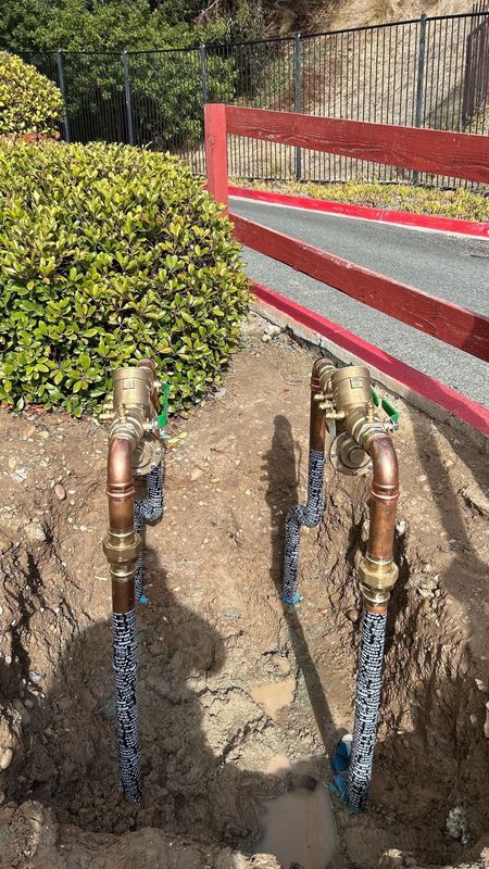 Pride Plumbing, Inc | A couple of copper pipes sitting in the dirt next to a fence.