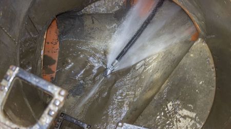 Pride Plumbing, Inc | A close up of a hose spraying water into a drain.