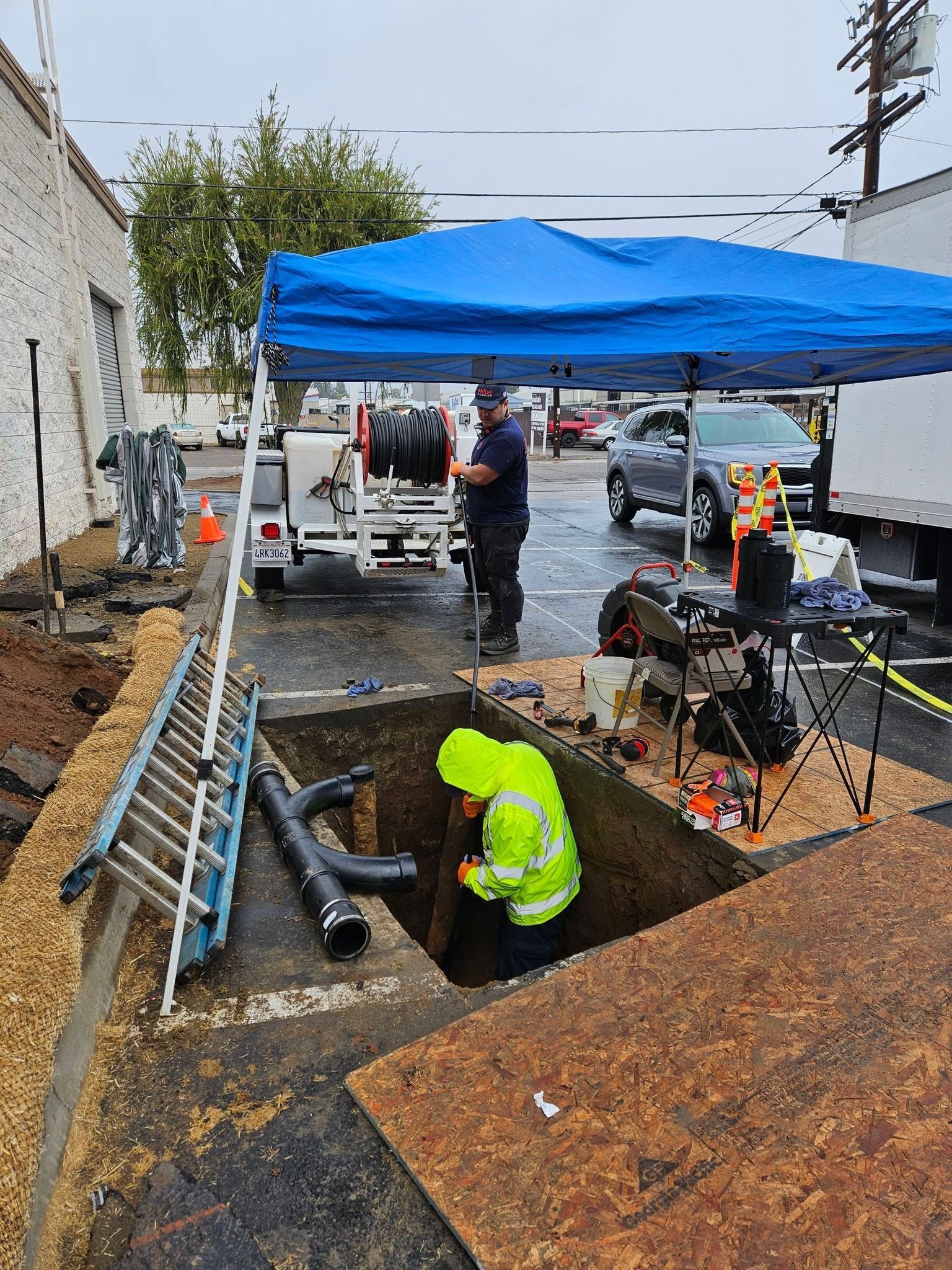 Pride Plumbing, Inc | A man is working in a hole in the ground under a blue tent.