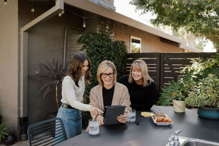 Three women are sitting at a table looking at a tablet.