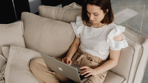 A girl sitting on the couch and using a Macbook device - Catricala Real Estate Group