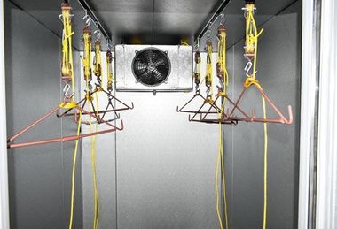 Interior of a test chamber with hanging yellow cables and red wire frames around a central fan