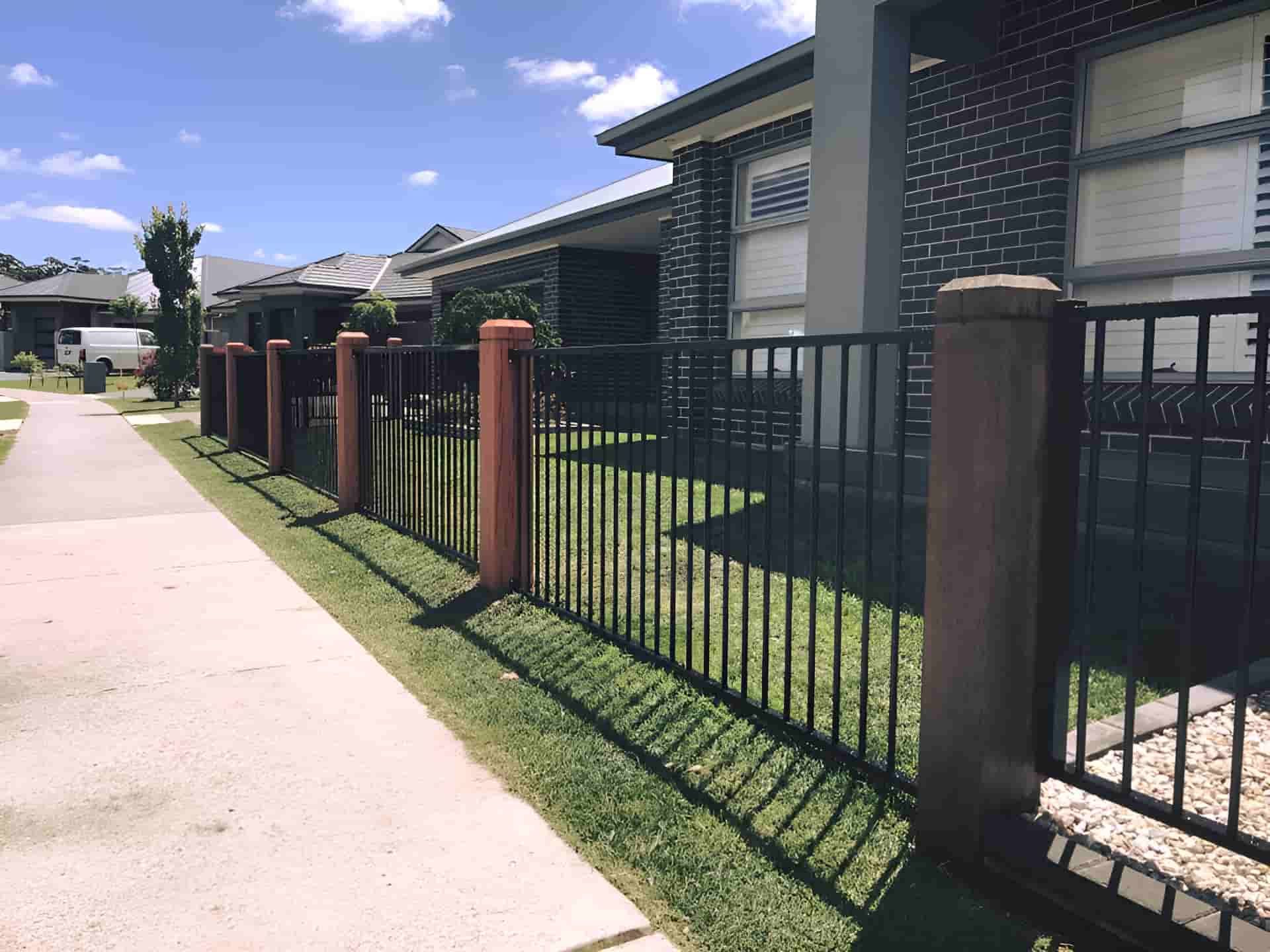 A Metal Fence Surrounds a Brick House in a Residential Area — A&H Fences In Aylmerton, NSW