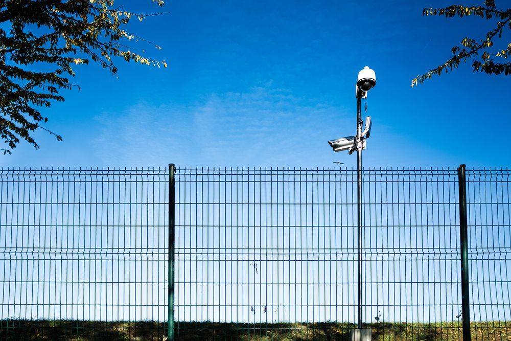 Security Cameras Atop a Pole Behind a Wire Fence, Blue Sky Backdrop — A&H Fences In Aylmerton, NSW