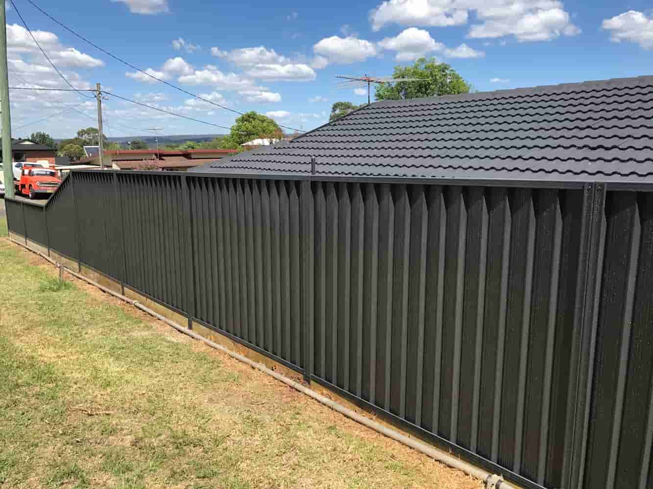 A Black Fence is Surrounding a House With a Tiled Roof — A&H Fences In Mittagong, NSW