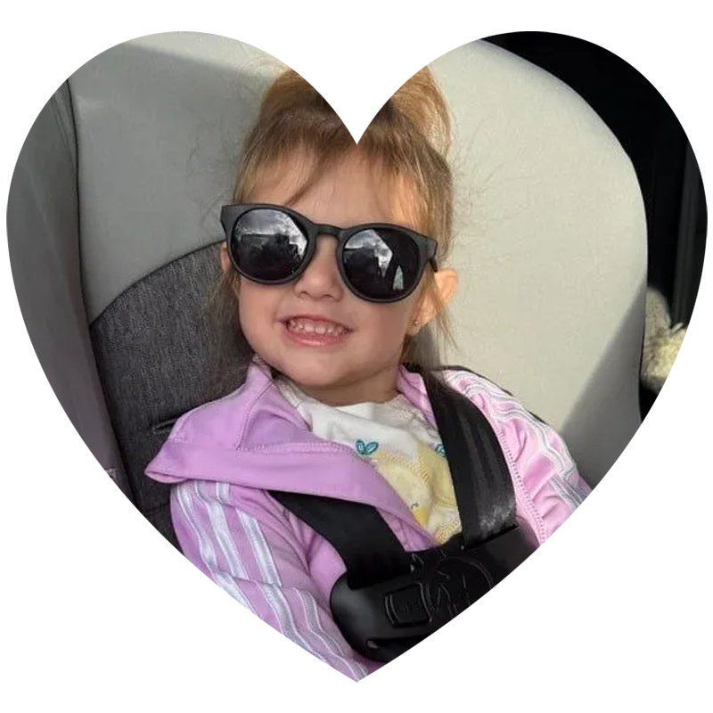 A little girl wearing sunglasses is sitting in a car seat holding a stuffed mickey mouse.