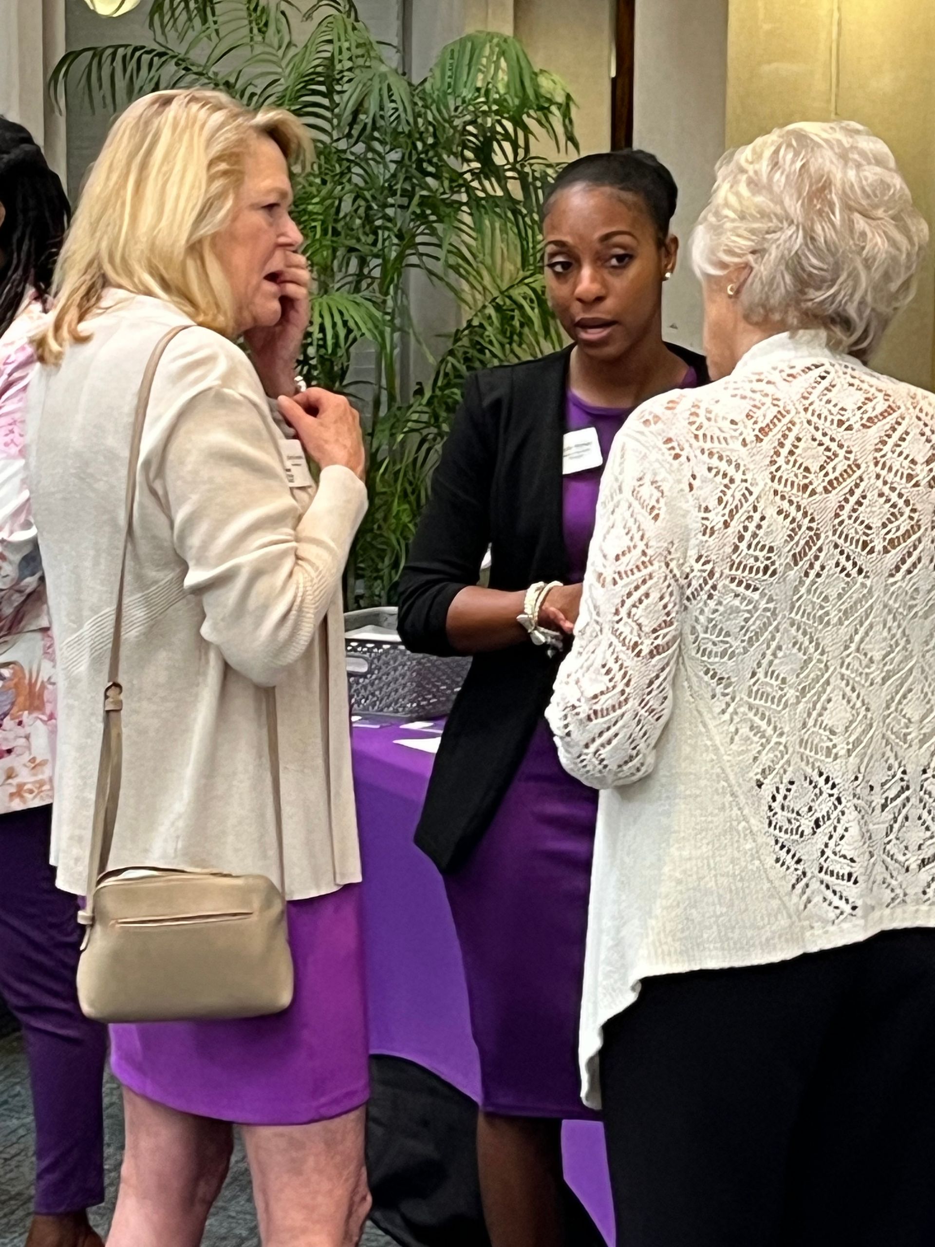 A group of women are standing around a table talking to each other.