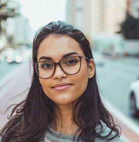 Woman with glasses smiling outdoors in front of a street.