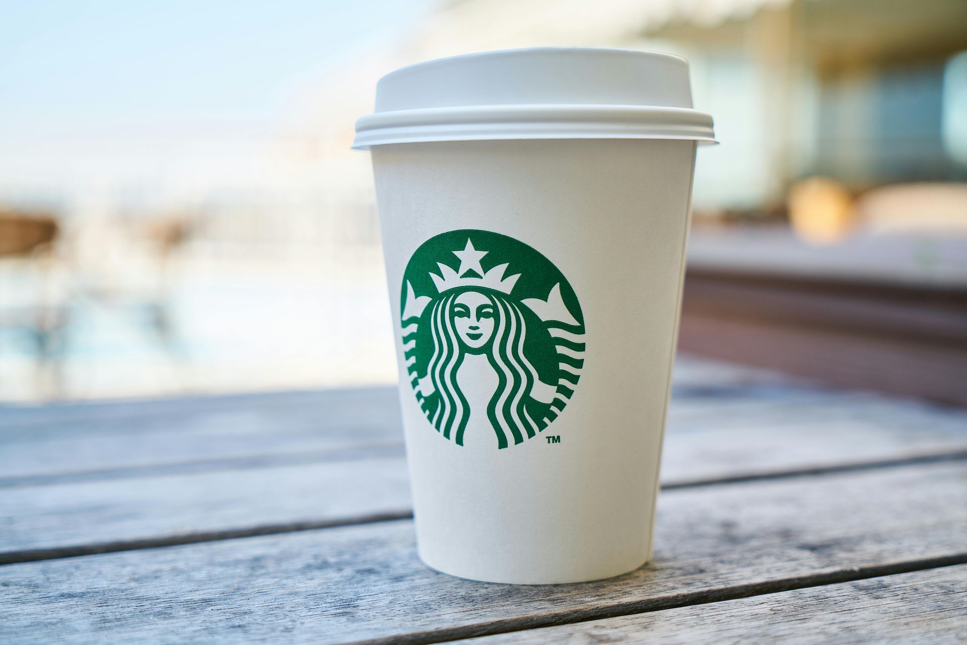 Starbucks coffee cup with green logo on a white paper cup, sitting on a weathered wooden table.
