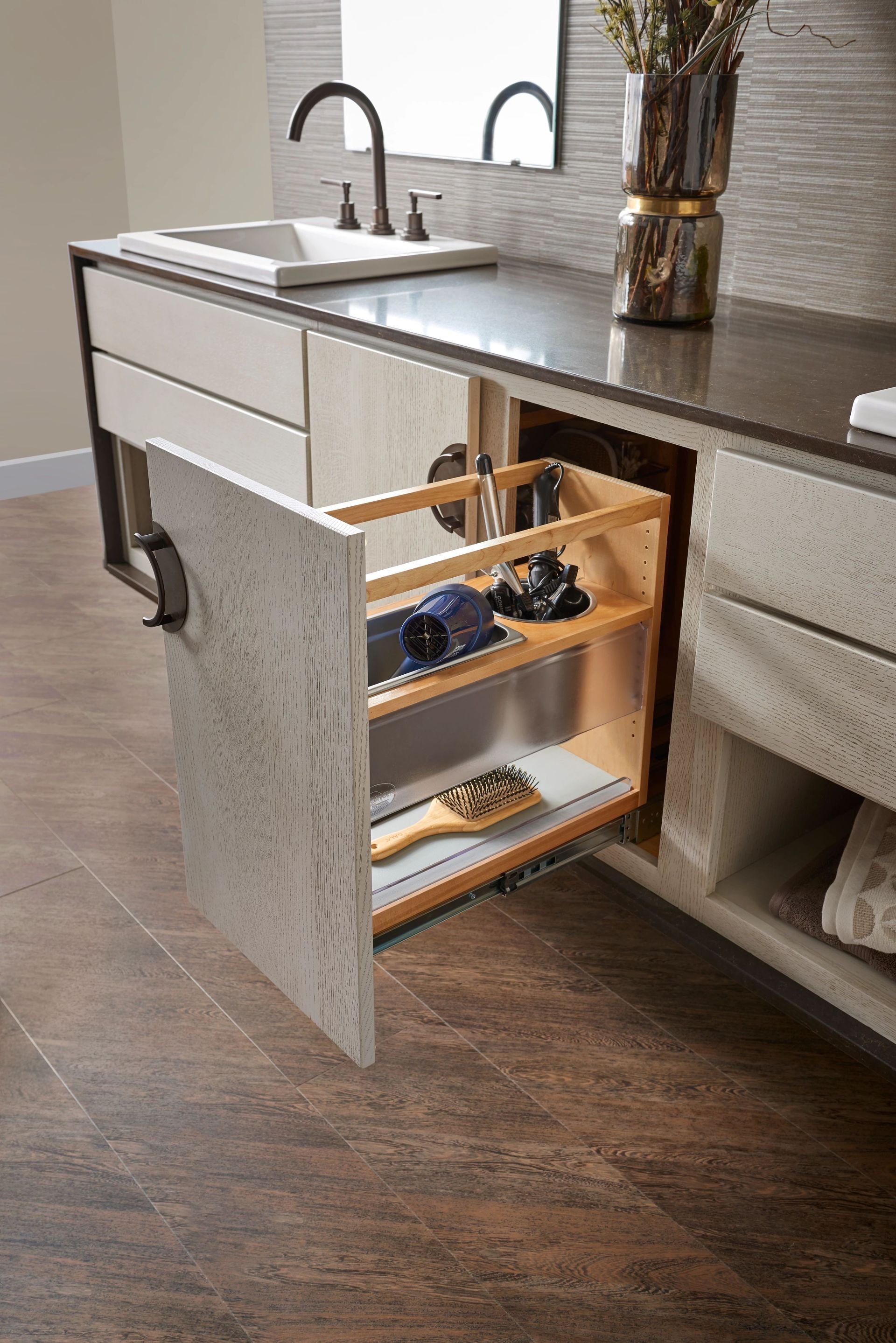 Bathroom cabinet with pull-out storage for grooming tools. Light wood tones with dark countertop and faucet.