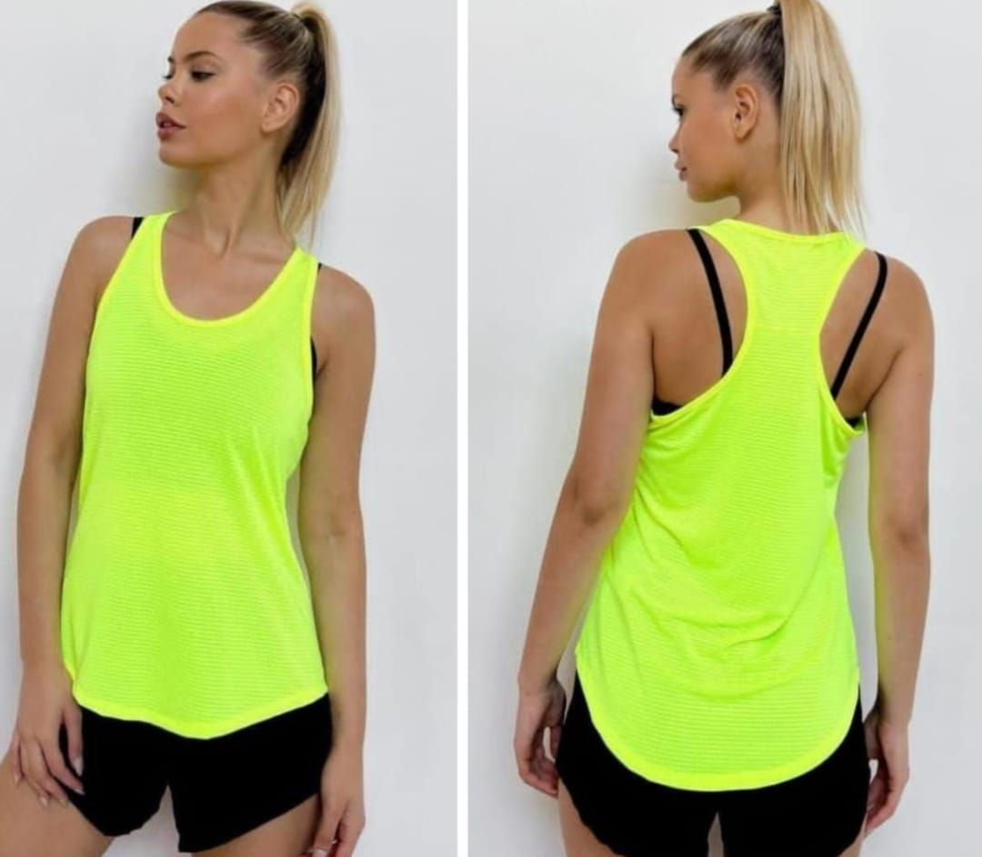 Mujer con camiseta sin mangas de entrenamiento de color amarillo neón y pantalones cortos negros, apoyada en una pared.