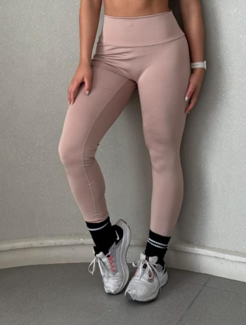 Mujer con leggings rosas, calcetines blancos y negros y zapatillas blancas, apoyada contra una pared.