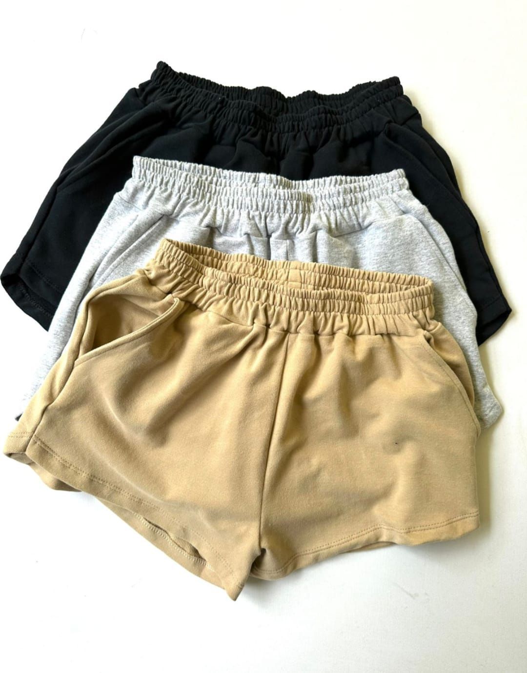 Tres pares de pantalones cortos de jersey, apilados. Negros, grises y tostados, todos con cinturilla elástica.