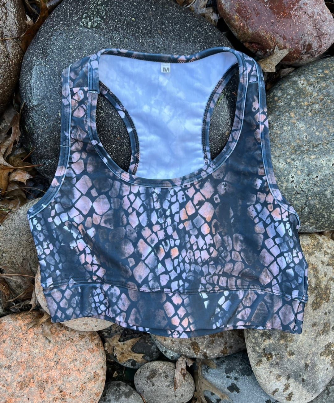 Sujetador deportivo de color oscuro con estampado de escamas de serpiente sobre un lecho de rocas.