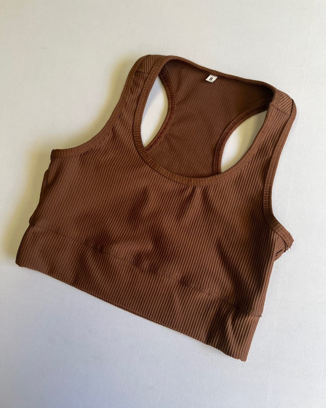 Sujetador deportivo con espalda cruzada, texturizado y de color marrón sobre una superficie blanca.