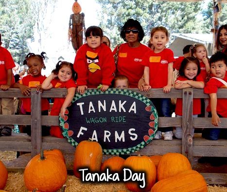 A group of children standing in front of a sign that says tanaka farms