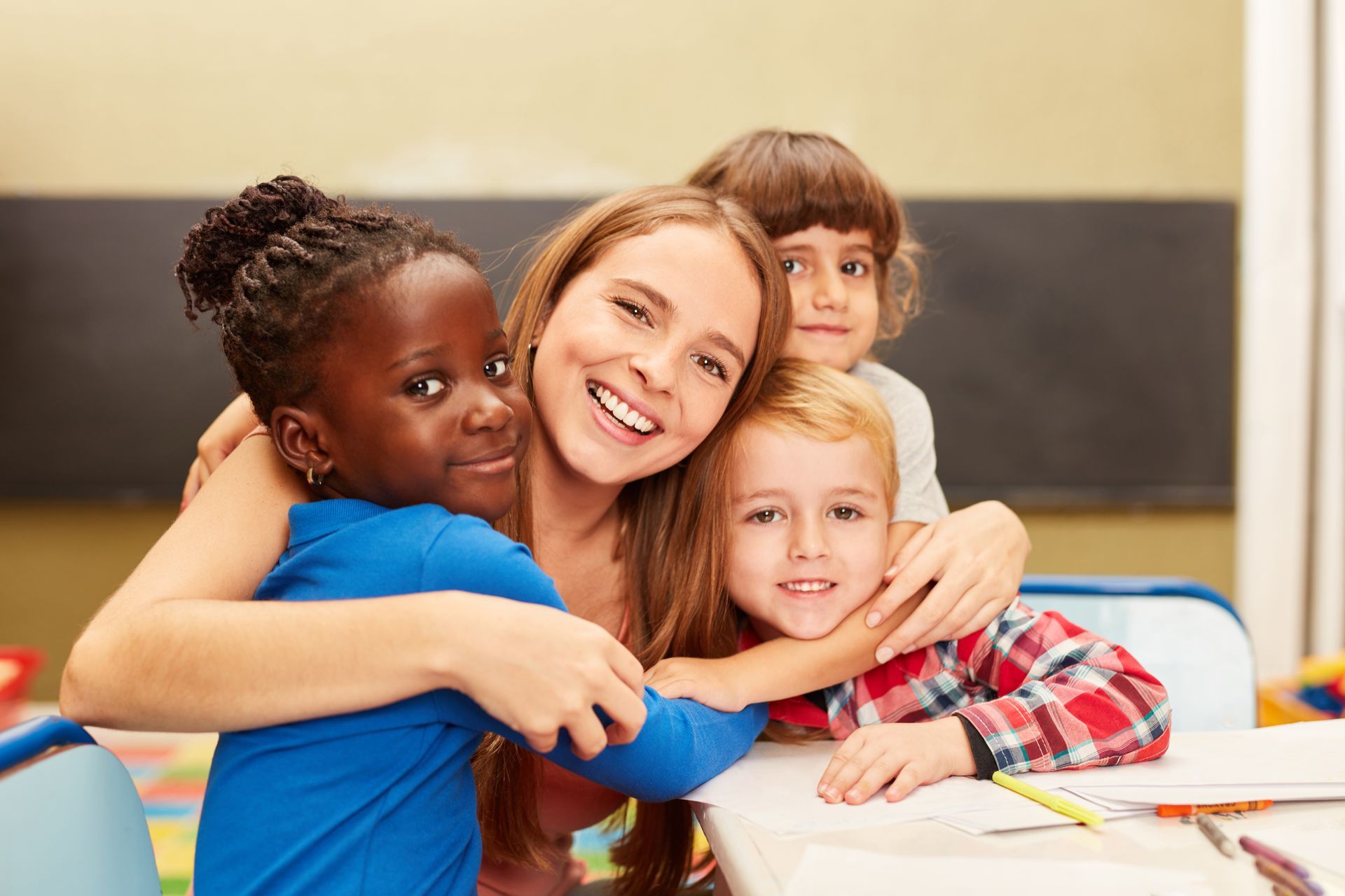 A teacher is hugging a group of children in a classroom.