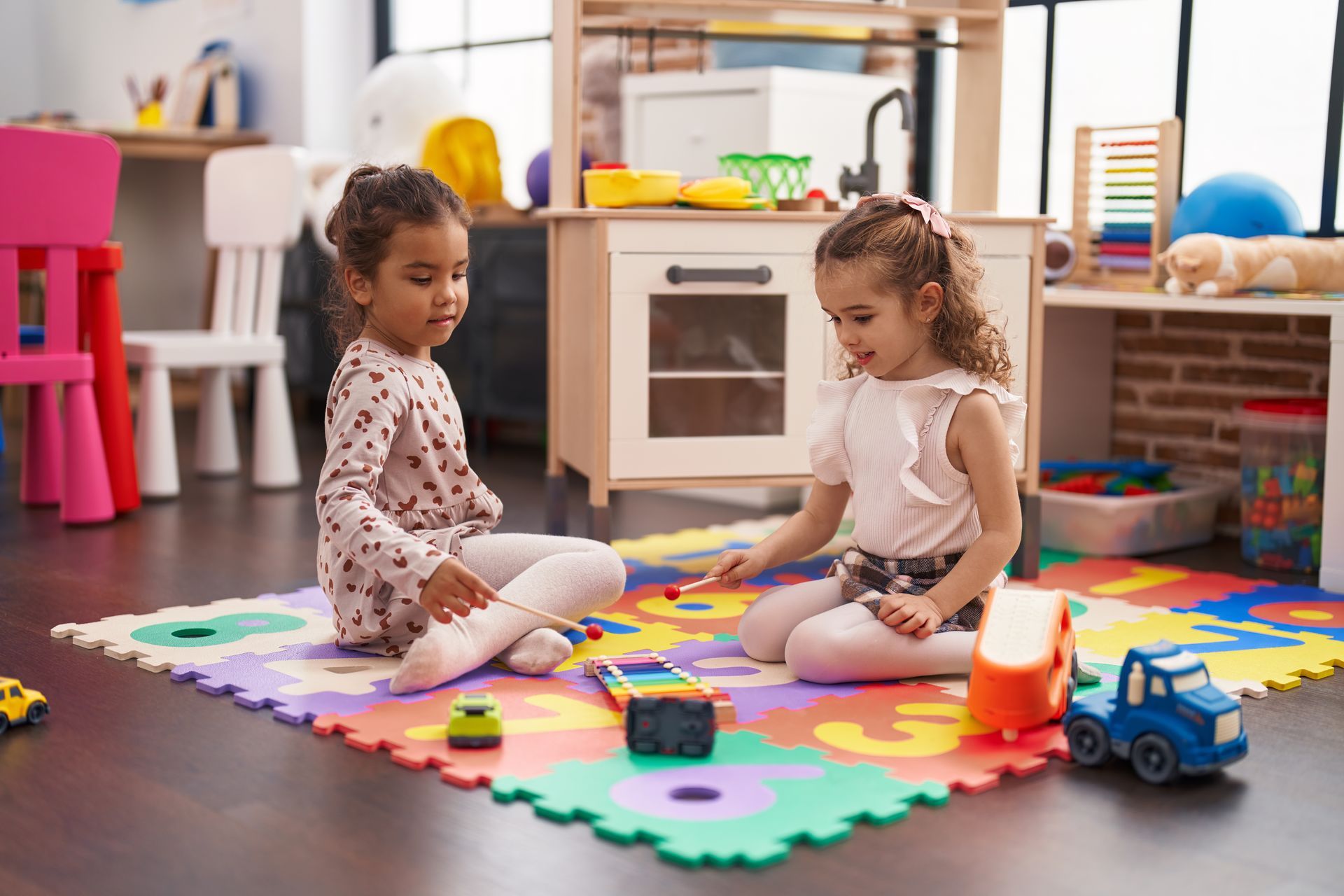 Two little girls are sitting on the floor playing with toys.