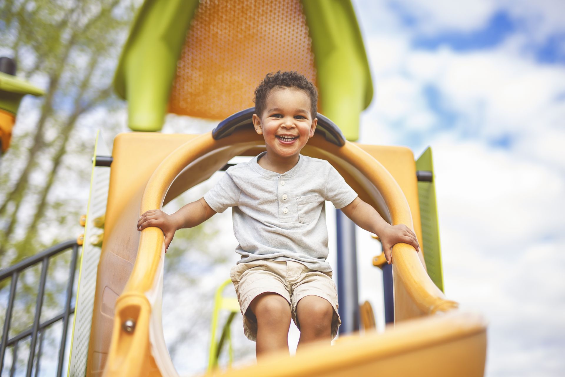 A young boy is sitting on a slide at a playground.