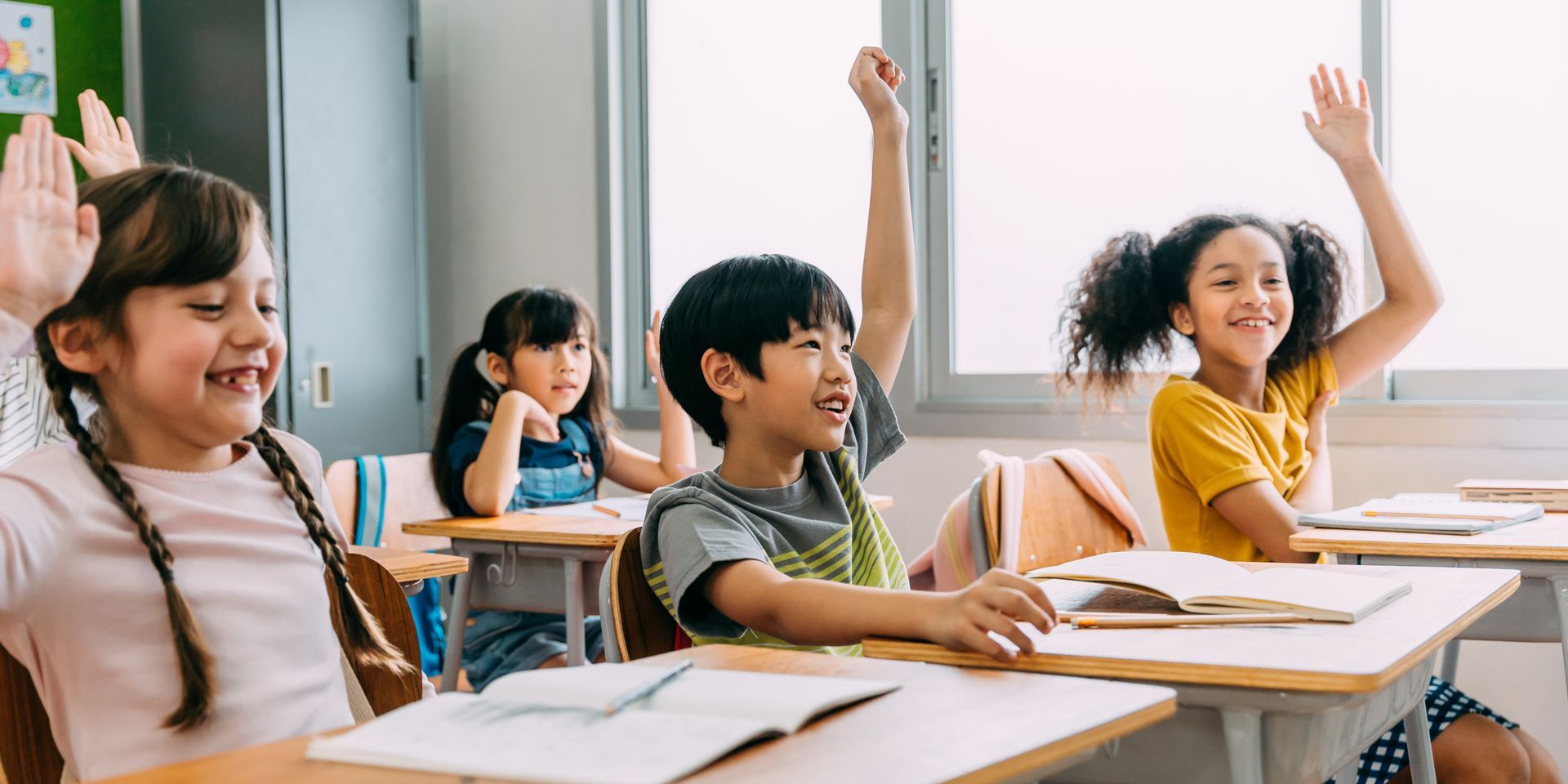 A group of children are raising their hands in a classroom.