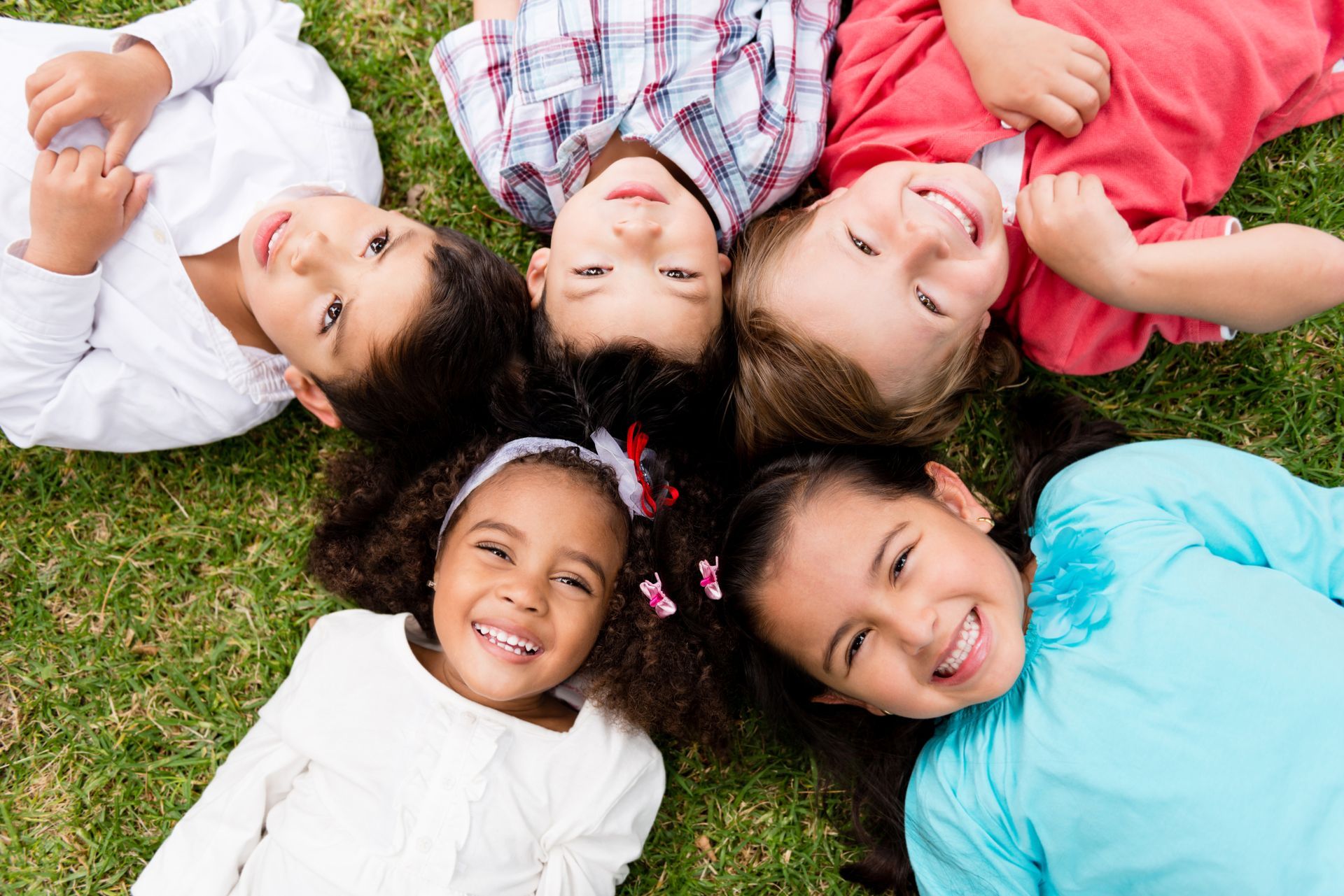 A group of children are laying in a circle on the grass.