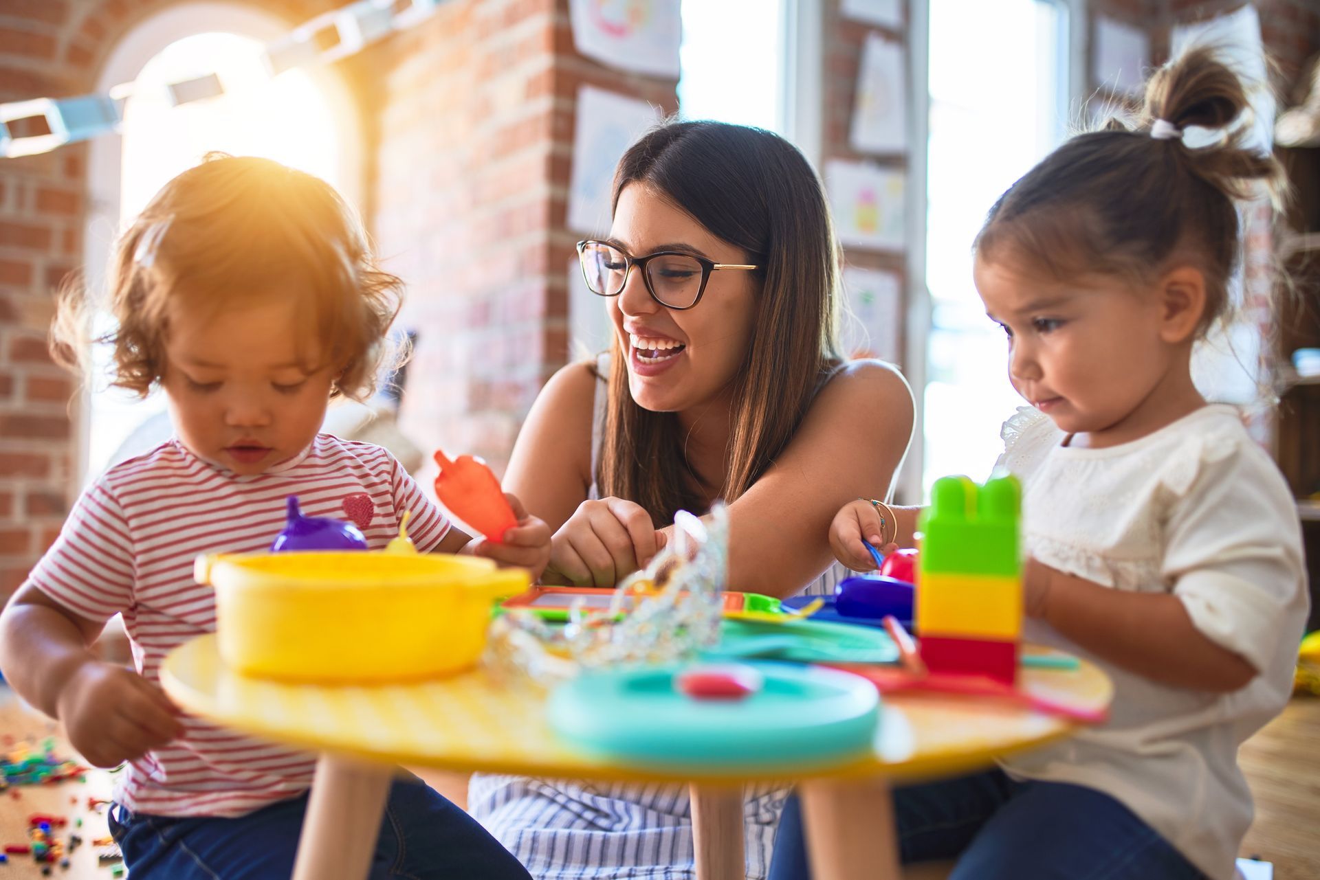 A woman is sitting at a table with two children playing with toys.