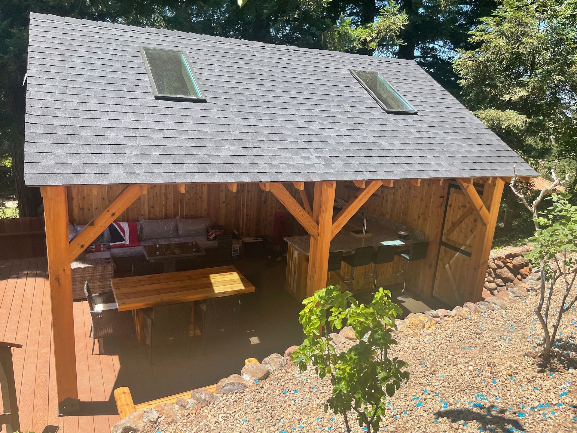 A wooden pavilion with a slate roof and a table and chairs underneath it.