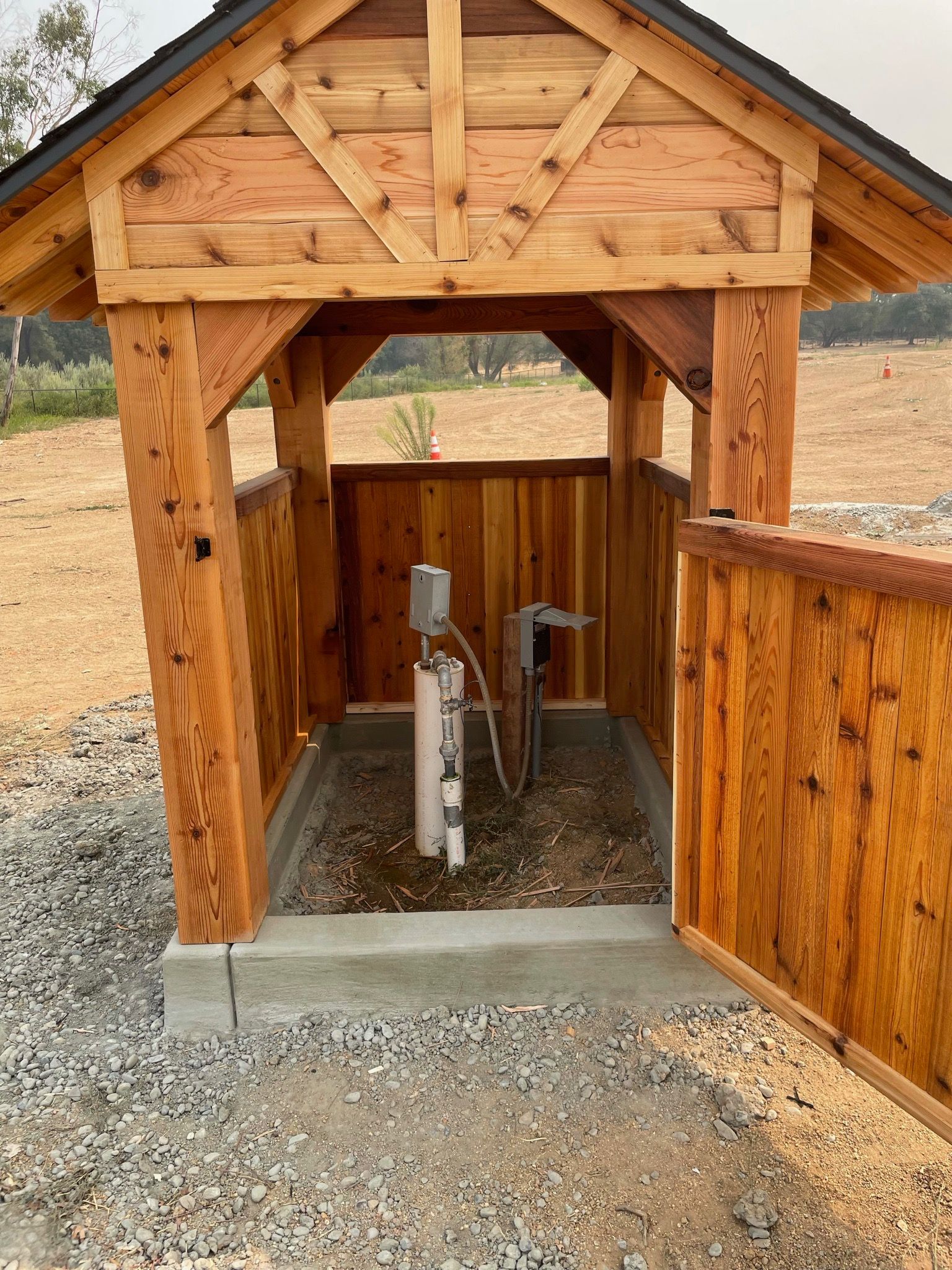 A wooden shelter with a water pump inside of it.
