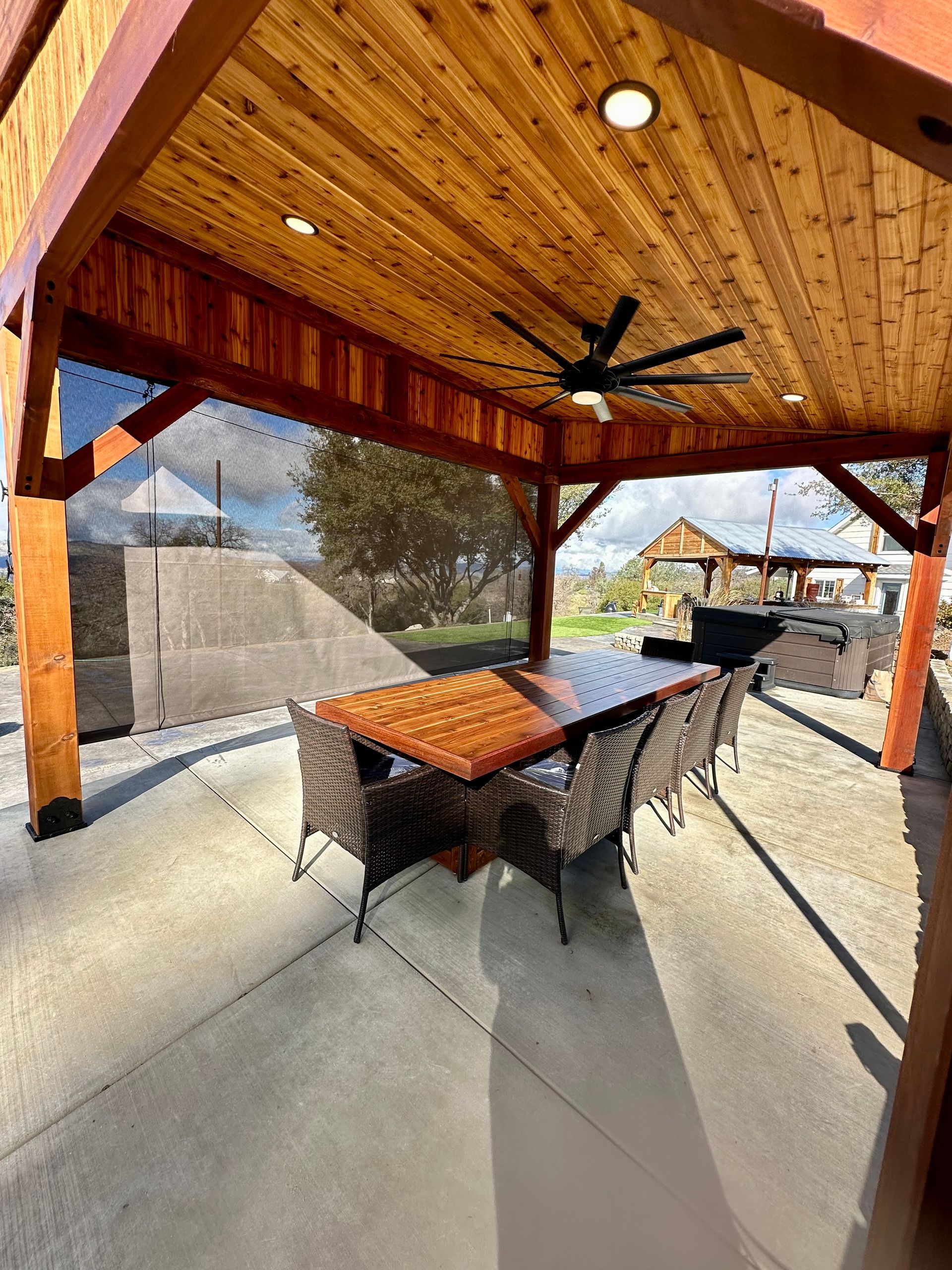 A wooden patio cover with a table and chairs underneath it.