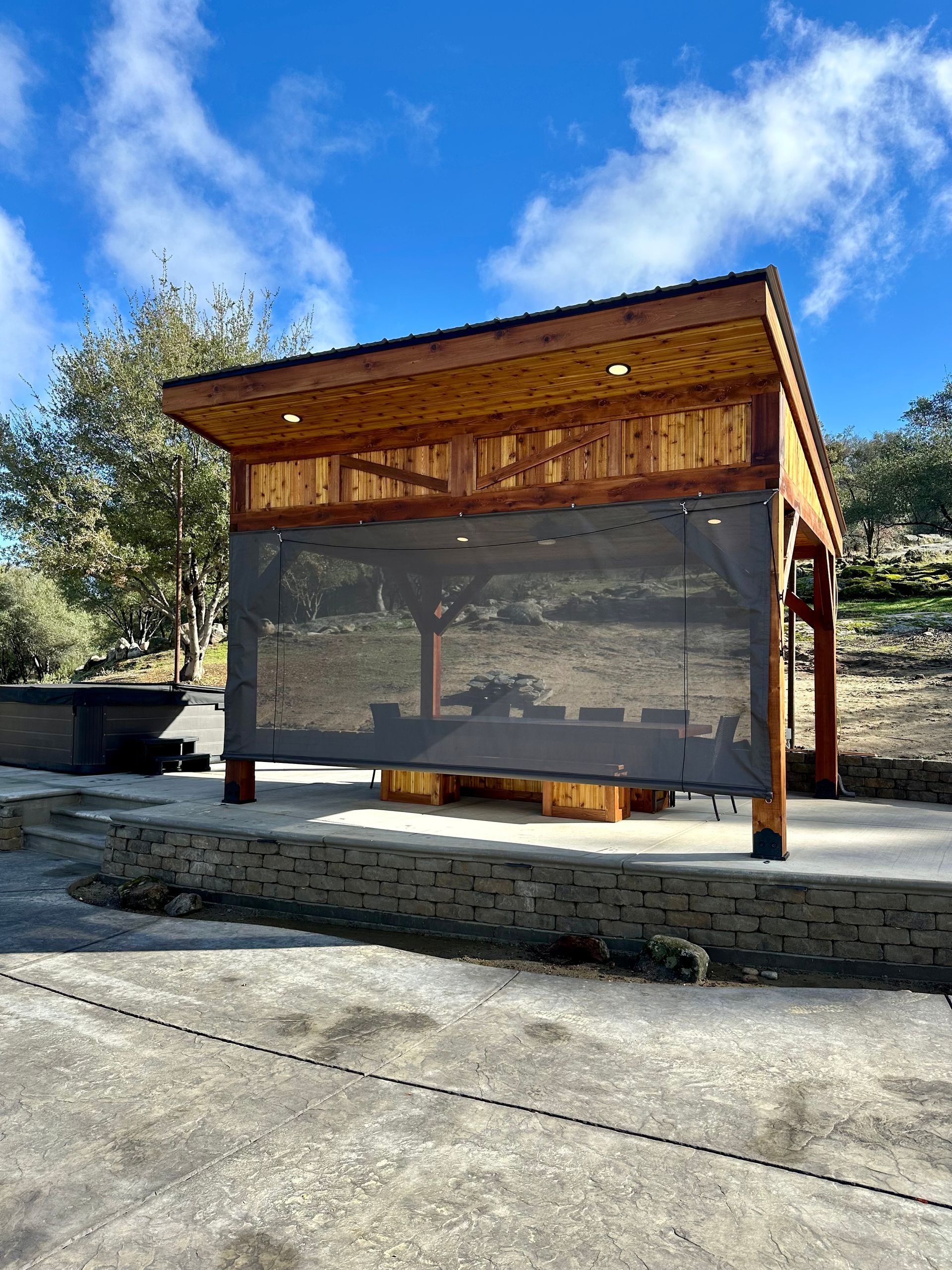 A wooden patio cover with a screen on the side of it.