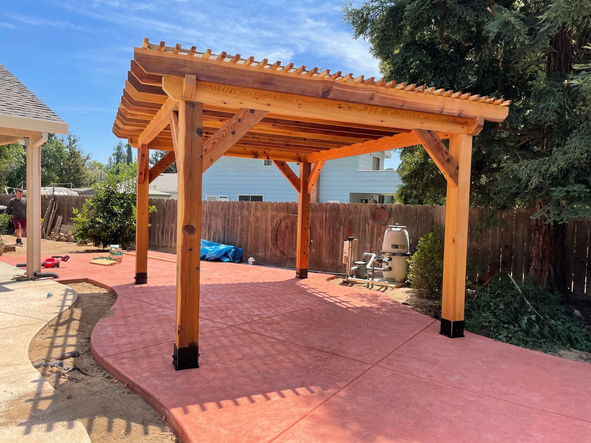 A wooden pergola is sitting on top of a red concrete patio.