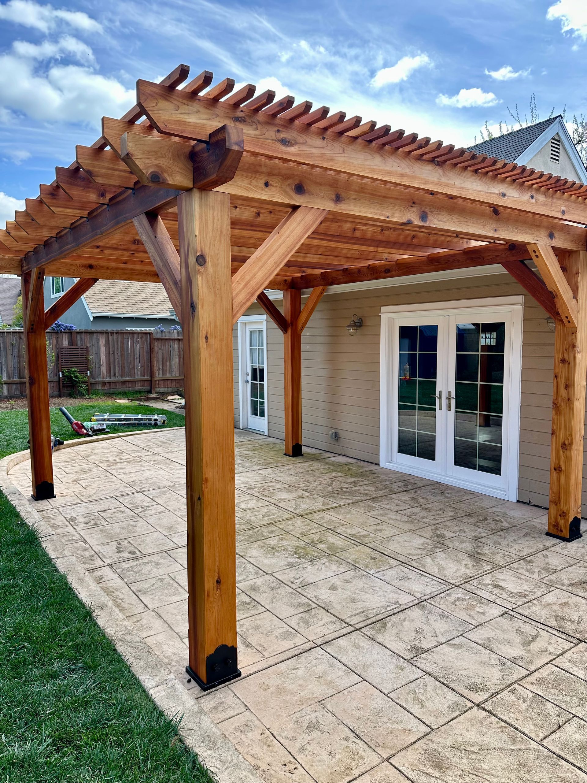 A wooden pergola is sitting on top of a patio next to a house.