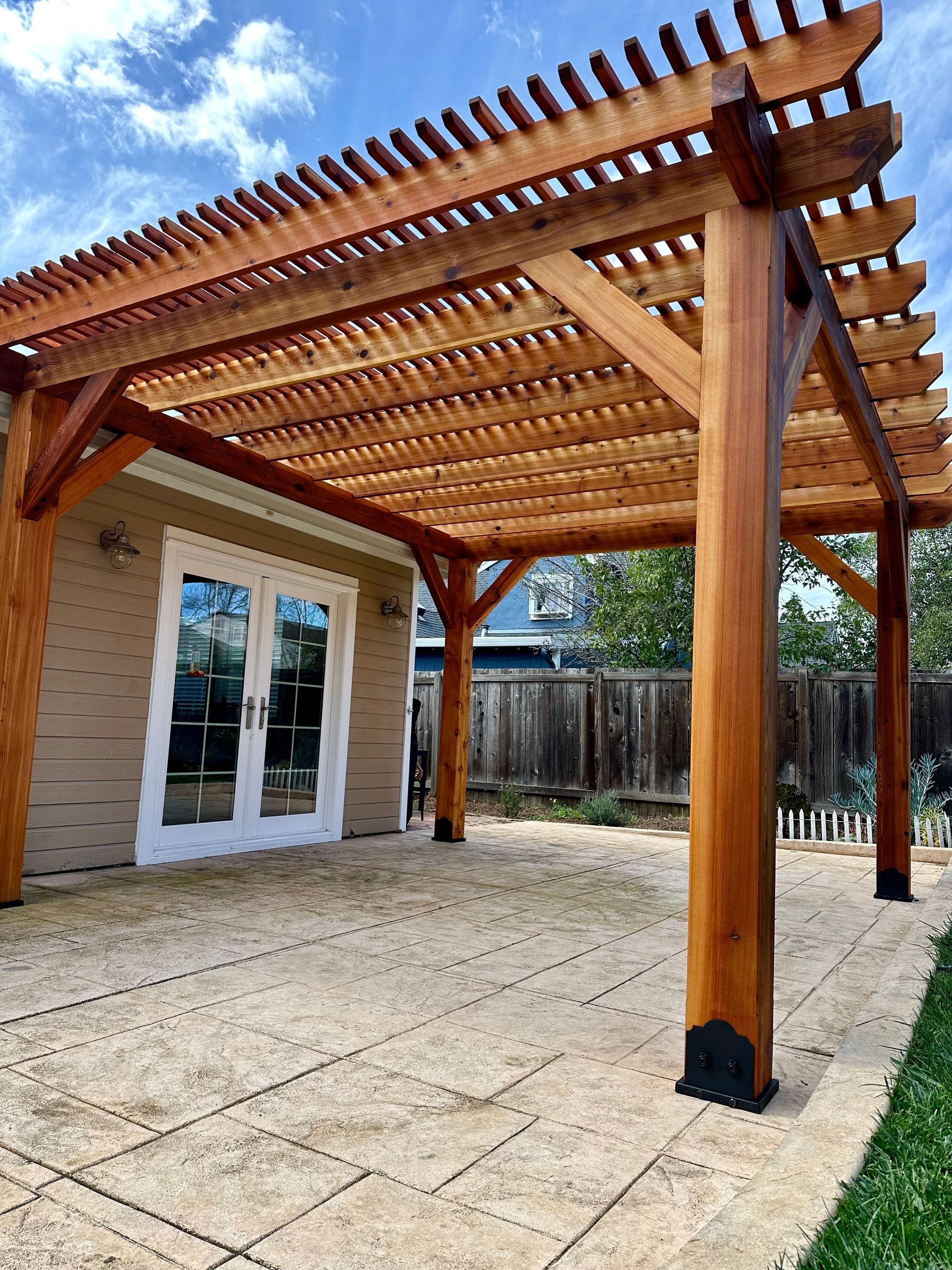 A wooden pergola is sitting on top of a patio next to a house.