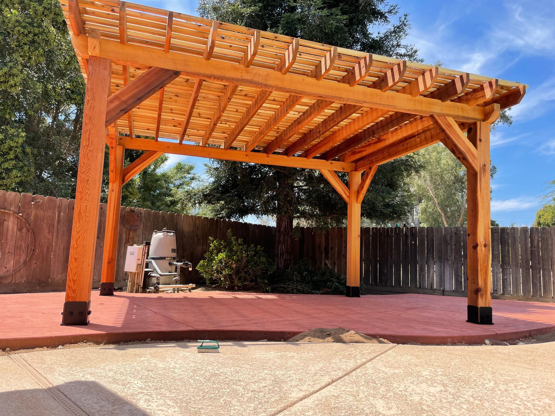 A wooden pergola is sitting on top of a concrete patio in a backyard.