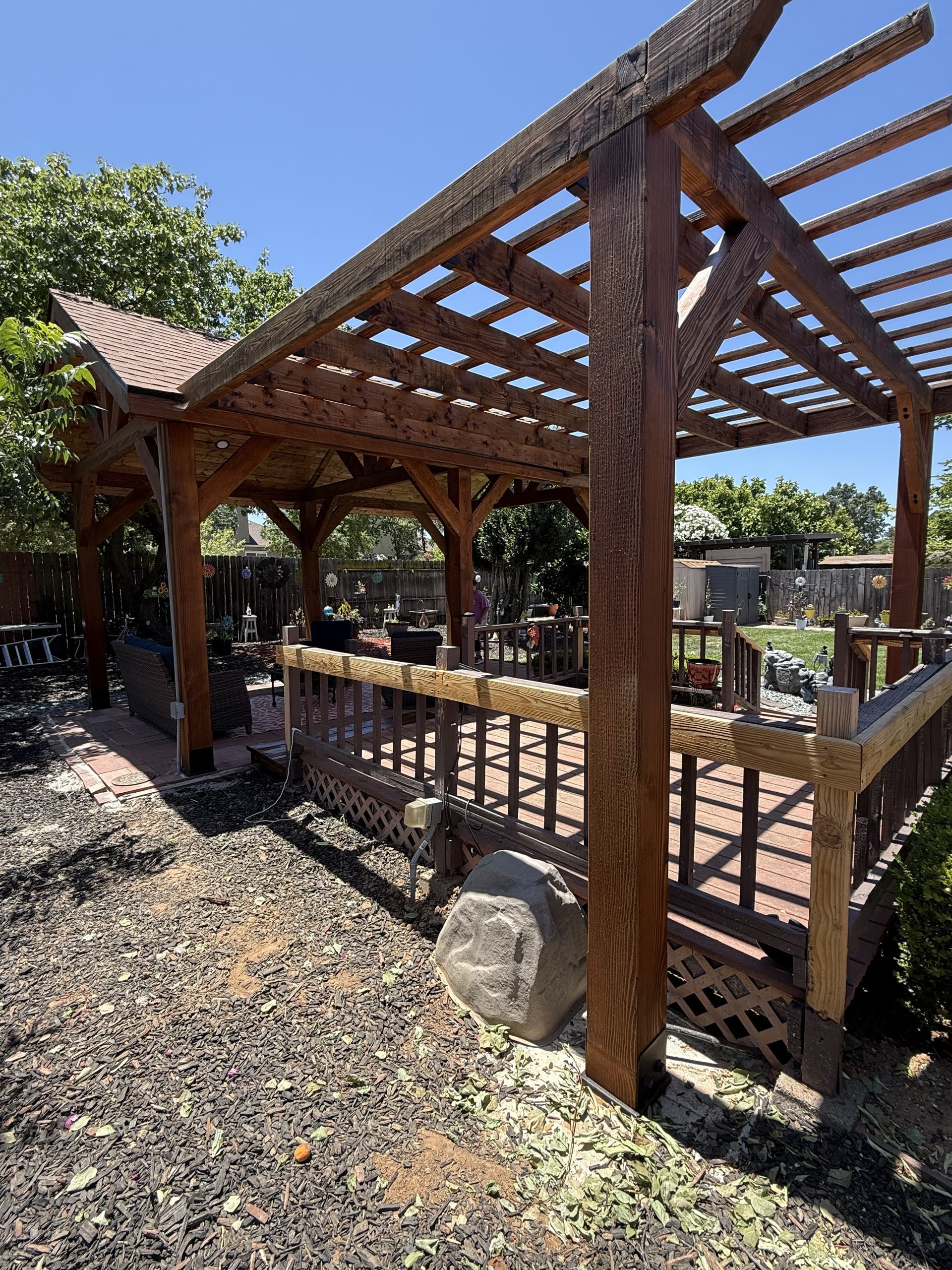 Wooden pergola with latticework, brown decking, and a surrounding gravel yard.