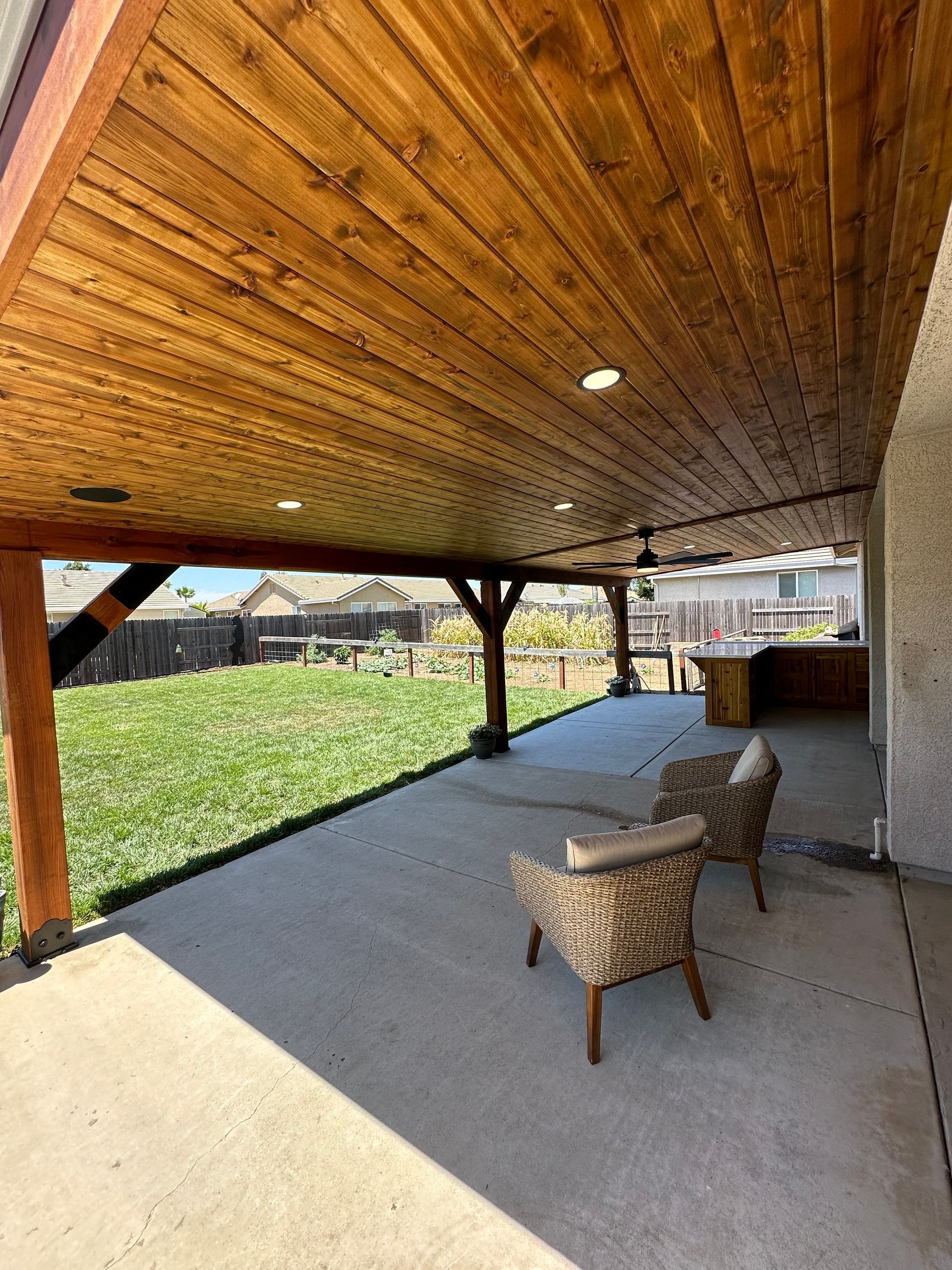 A covered patio with a wooden ceiling and chairs.