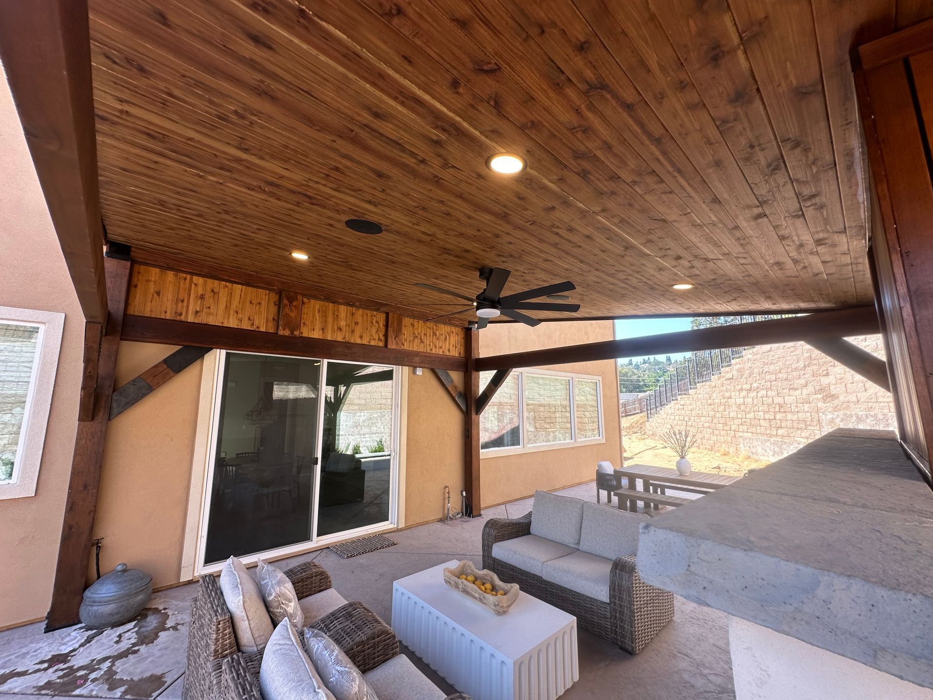 A patio with a couch , chair , table and ceiling fan.