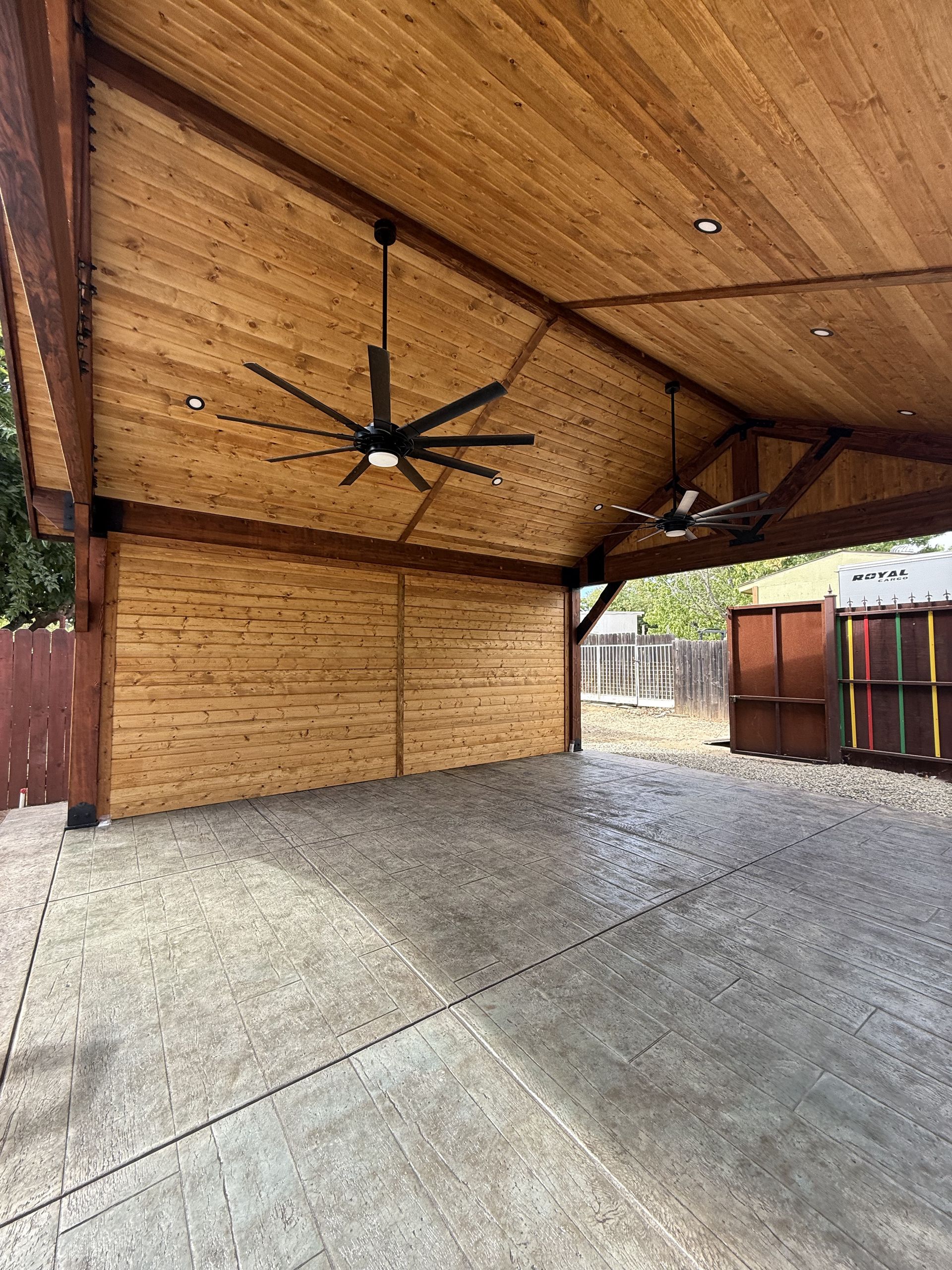 Covered pavilion with a wooden ceiling, concrete floor, and ceiling fan.