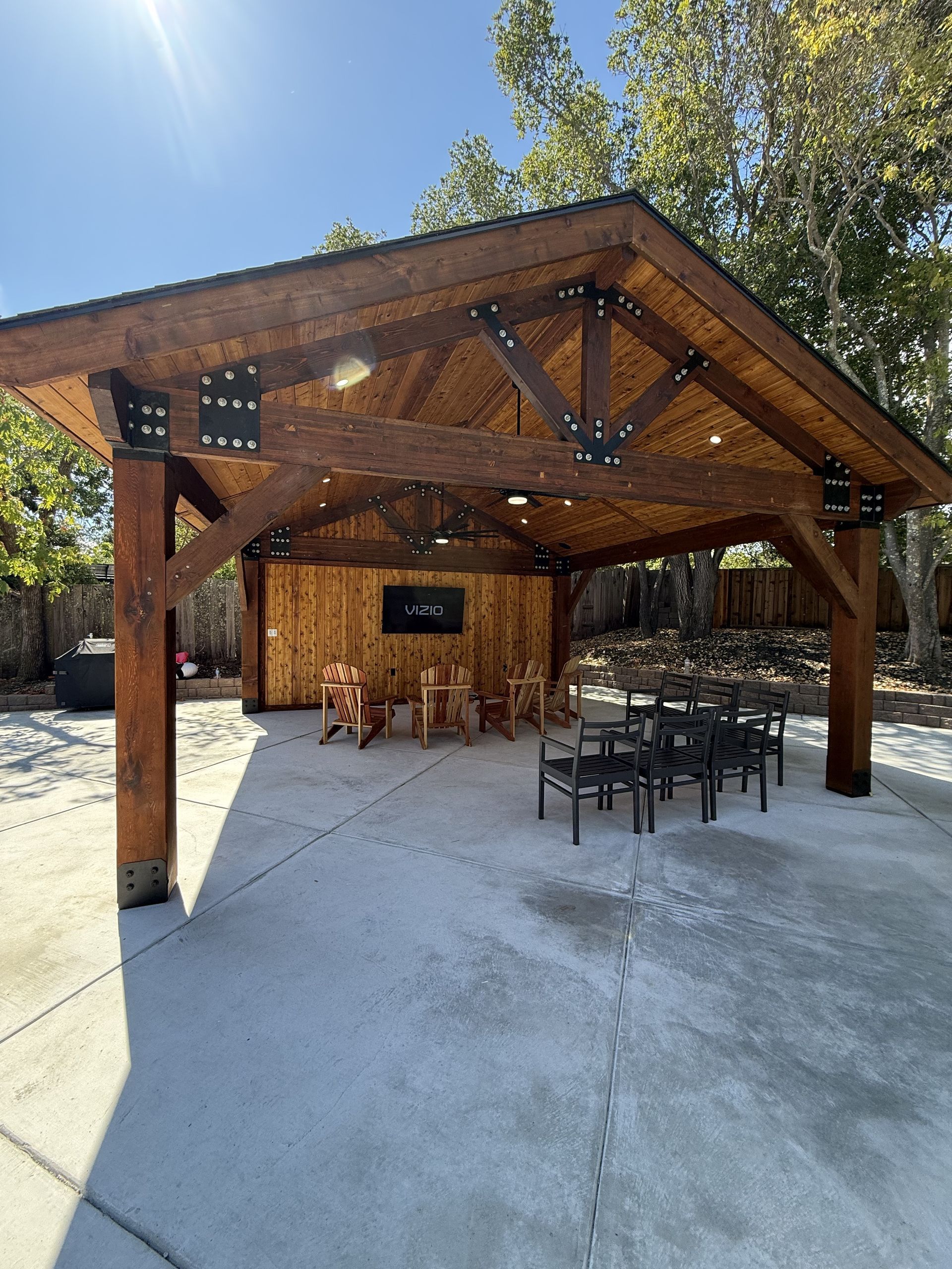 Wooden pavilion with a concrete patio, seating, and built-in lighting.