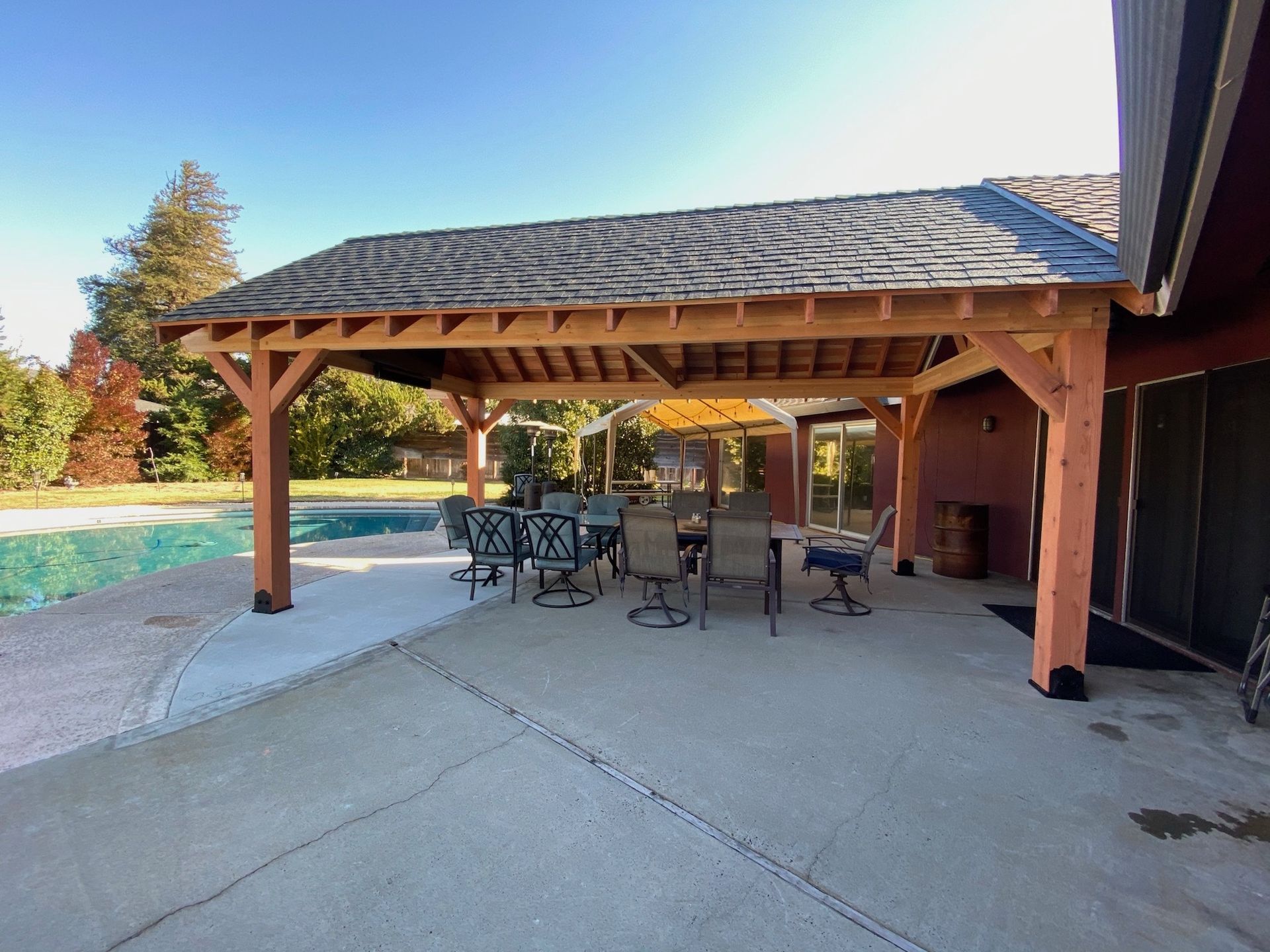 A patio with a table and chairs under a pavilion next to a pool.