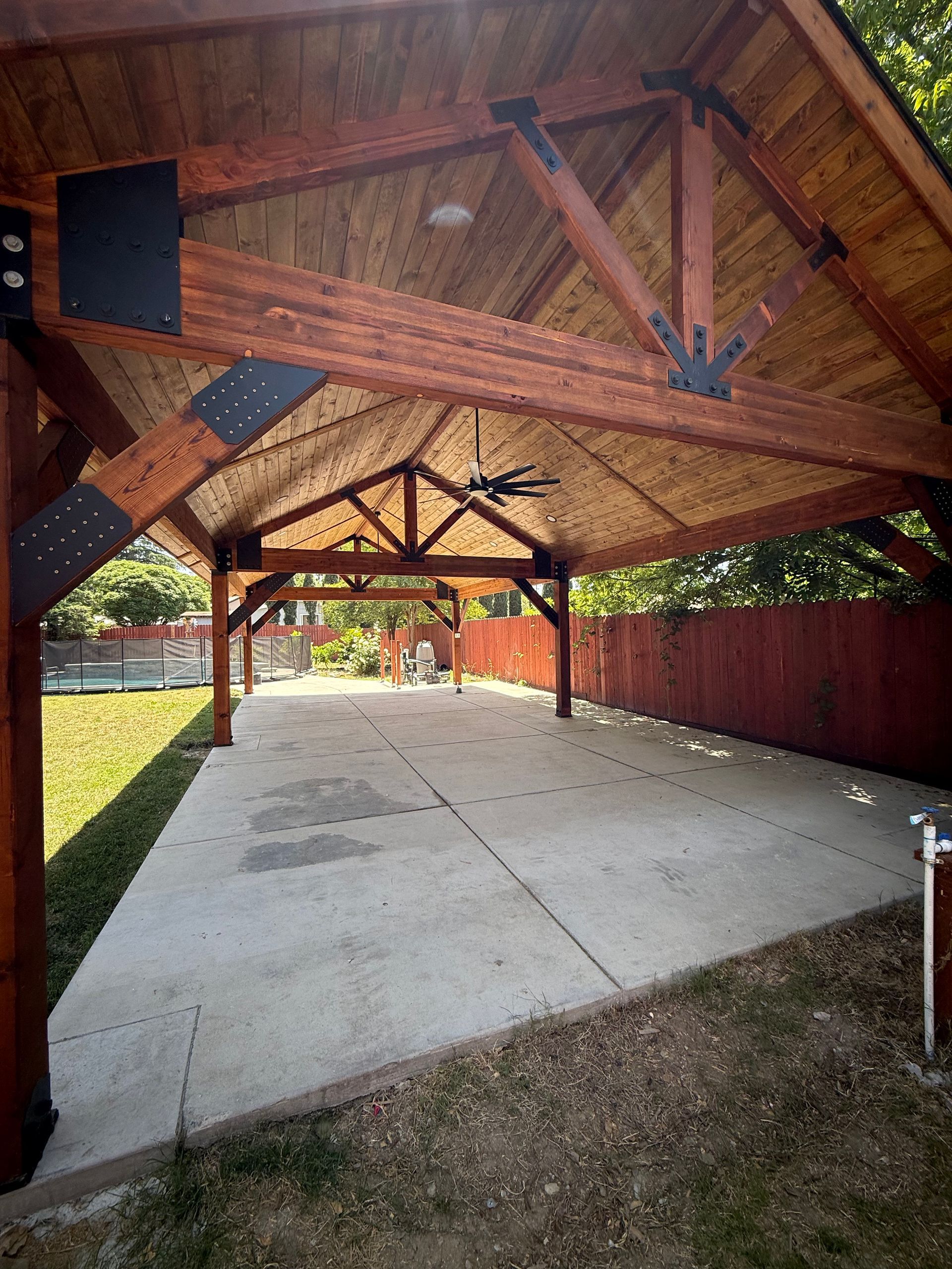Wooden pavilion with concrete floor in a yard, dark brown beams, black accents.