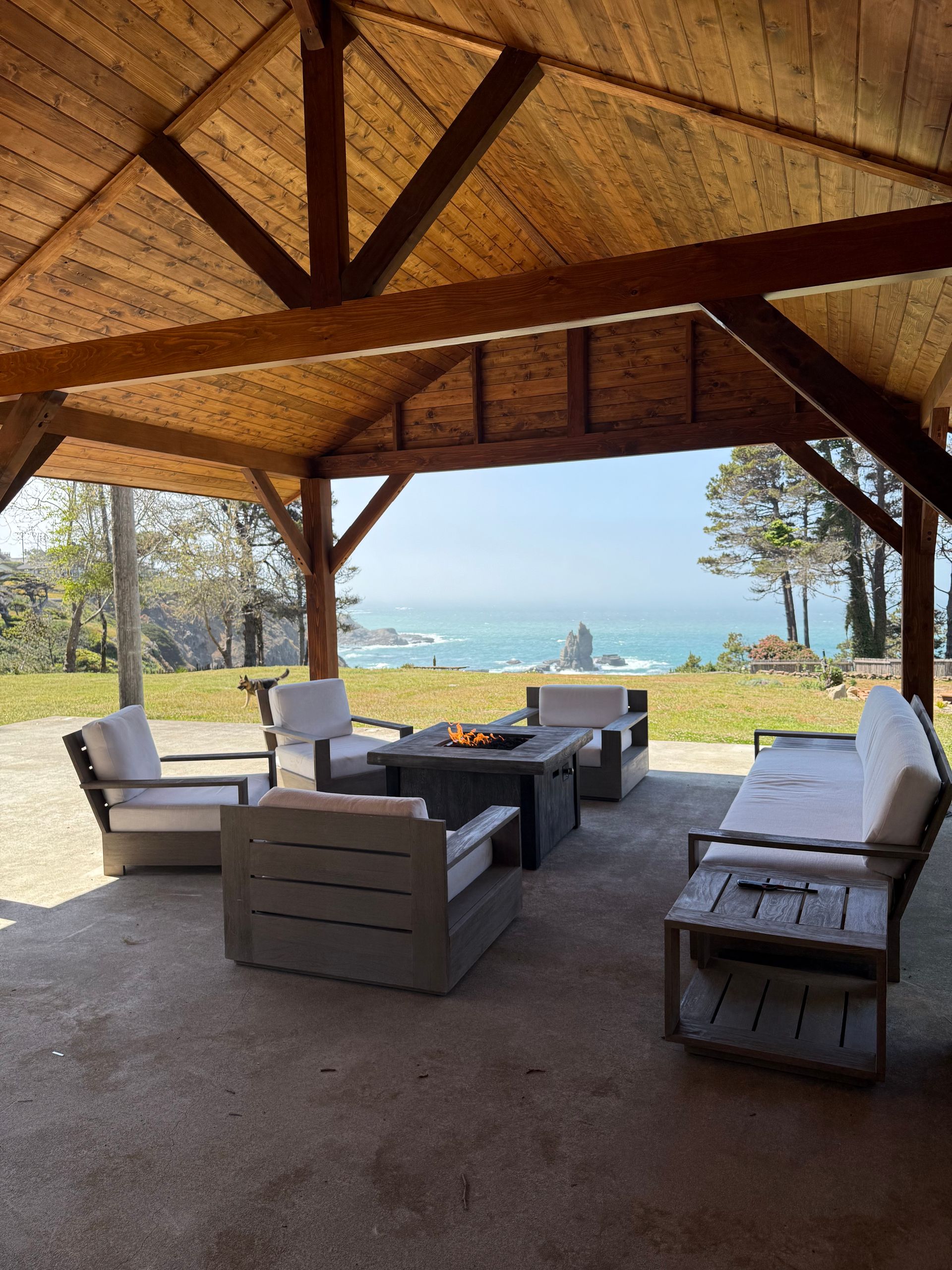 Outdoor seating area under a wooden pavilion overlooking the ocean; light-colored furniture.